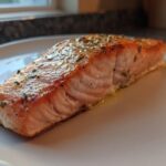 Close-up of a perfectly cooked, flaky air fryer salmon fillet seasoned with herbs on a white plate.