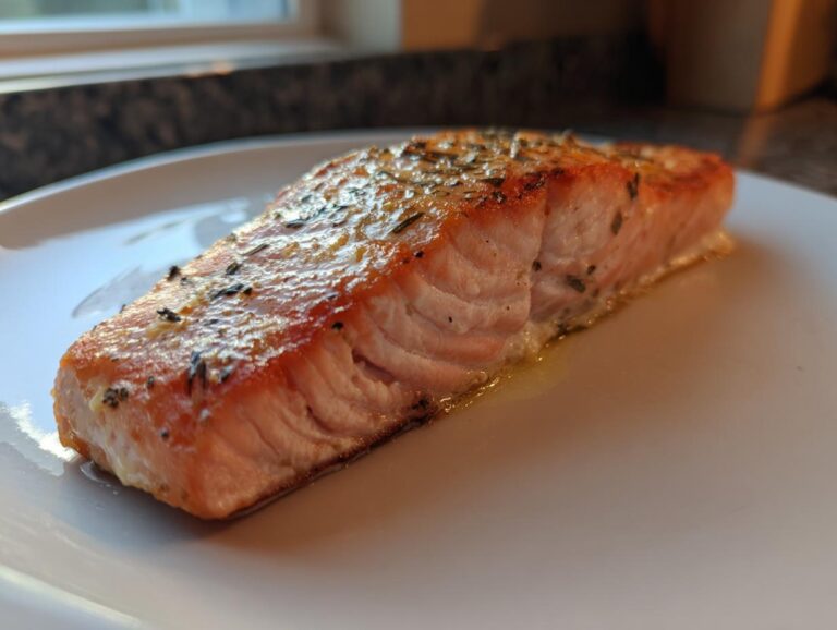Amazing 10-Minute Air Fryer Salmon Secret Close-up of a perfectly cooked, flaky air fryer salmon fillet seasoned with herbs on a white plate.