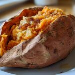 Close-up of a fluffy baked sweet potatoes, split open and seasoned on a white plate.