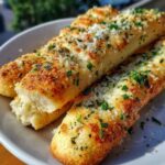 Close-up of three golden brown breadsticks topped with melted cheese, grated Parmesan, and fresh parsley.