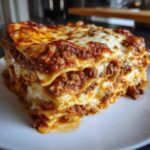 A thick, multi-layered slice of amazing lasagna featuring rich meat sauce and melted cheese on a white plate.