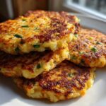 A stack of four perfectly golden brown mashed potato cakes, flecked with green chives, sitting on a white plate.