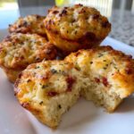 A close-up of several golden-brown Pizza Muffins, one broken open to show the soft interior and pepperoni pieces.