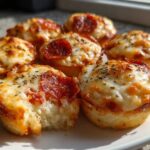 A plate of freshly baked, cheesy pepperoni pizza muffins, one of which has a bite taken out.