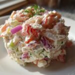 A close-up, molded serving of creamy seafood salad featuring shrimp, celery, and red onion, garnished with dill.