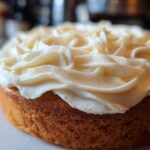Close-up of a golden cake topped with thick, beautifully piped swirls of rich cream cheese frosting.