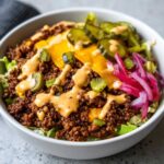 Close-up of a cheeseburger bowl featuring seasoned ground beef, melted cheese, pickles, and special sauce over lettuce.