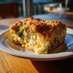 A square slice of creamy broccoli casserole with a golden brown crumb topping, served on a white plate.
