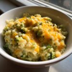 Close-up of creamy broccoli rice topped with melted cheddar cheese served in a white bowl.