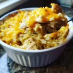 A spoonful of creamy, cheesy chicken and rice being lifted from a white ramekin dish.