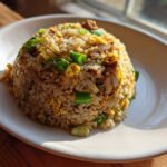 A mound of savory chicken fried rice mixed with scrambled egg and green onions served on a white plate.