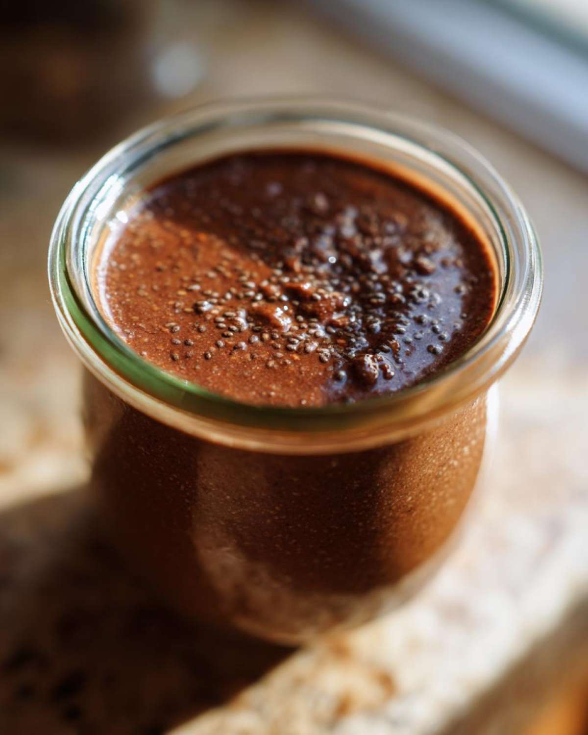 Close-up of rich, brown chocolate overnight oats topped with visible chia seeds in a glass jar.