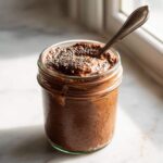 A glass jar filled with creamy chocolate overnight oats, topped with chia seeds and a spoon.