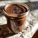 Close-up of rich chocolate overnight oats topped with chia seeds in a glass mason jar.