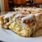 Close-up of several gooey servings of Cinnamon roll casserole topped with white icing, sitting on a white plate.