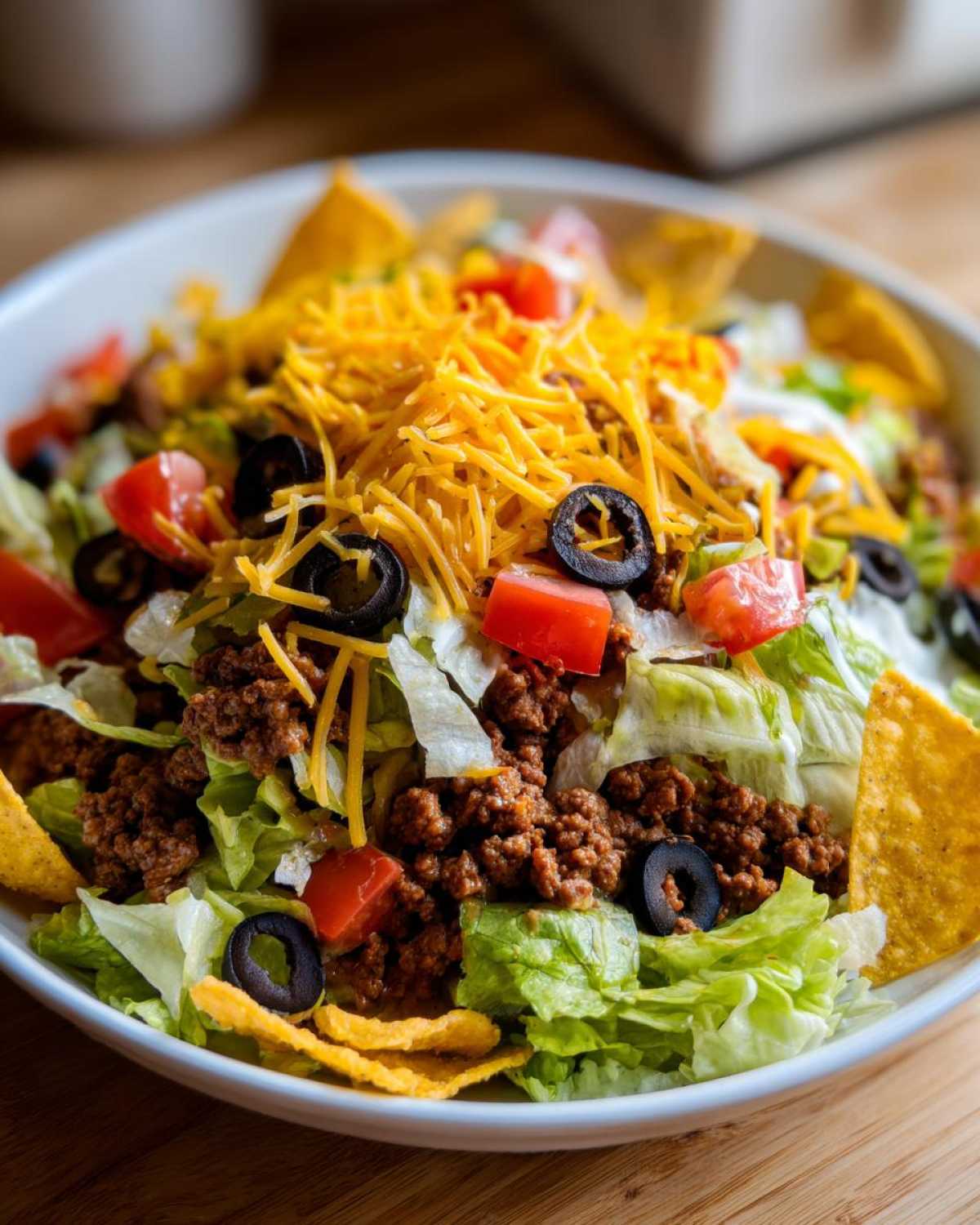 A close-up view of a hearty taco salad featuring seasoned ground beef, shredded lettuce, tomatoes, black olives, and shredded cheese.