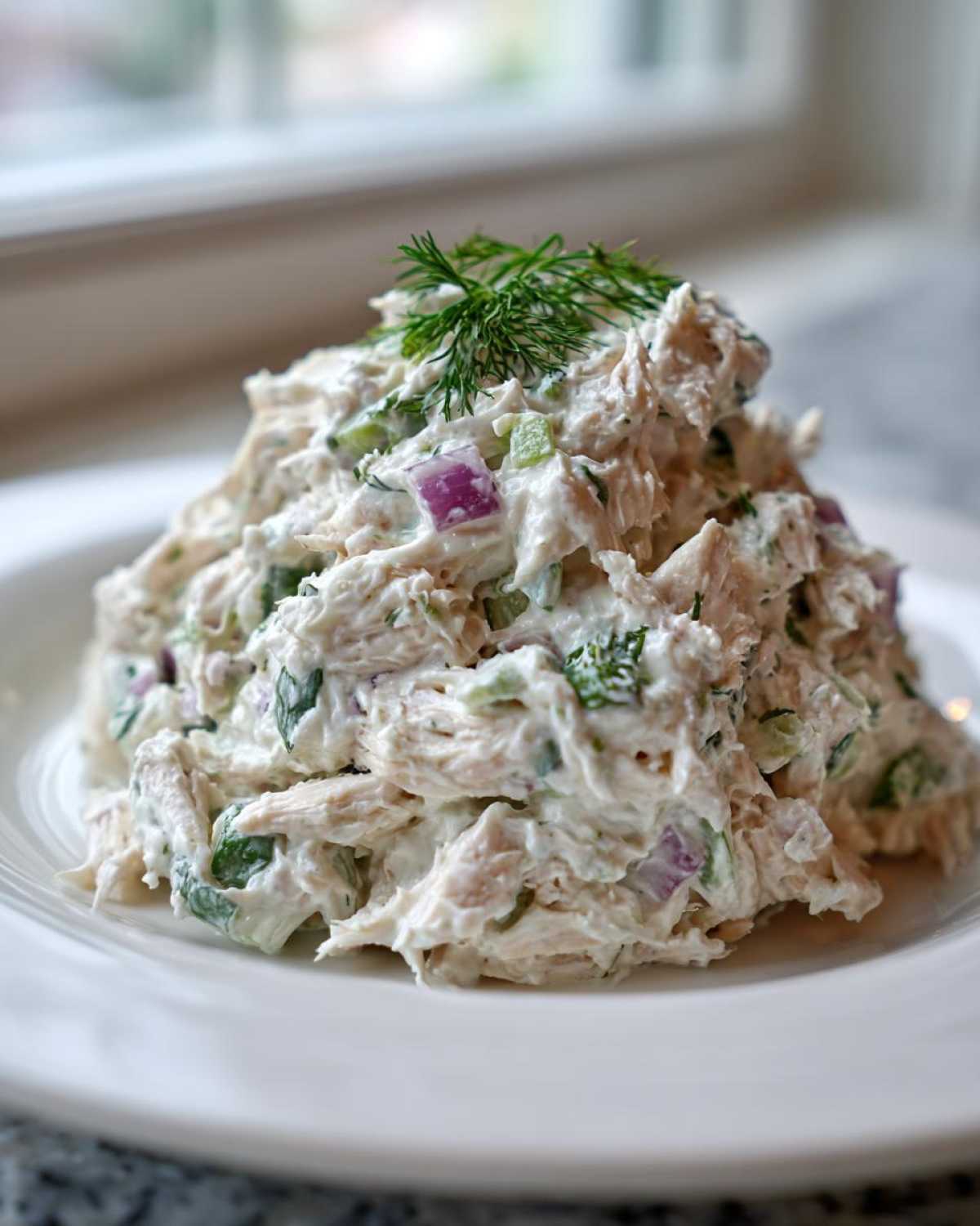 A generous mound of creamy cottage cheese chicken salad mixed with red onion and celery, garnished with fresh dill.