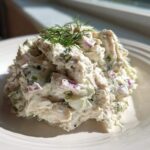 A scoop of creamy cottage cheese chicken salad mixed with red onion and celery, garnished with fresh dill.