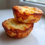 Two golden-brown cottage cheese egg cups stacked on a white surface, showing a fluffy interior.
