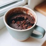 A rich, dark chocolate Cottage Cheese Microwave Brownie topped with melted chocolate chunks in a light blue mug.