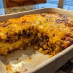 A baked cowboy cornbread casserole with a thick layer of melted cheddar cheese and ground beef filling visible.
