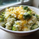 Close-up of a creamy bowl of broccoli rice topped with melted cheddar cheese.