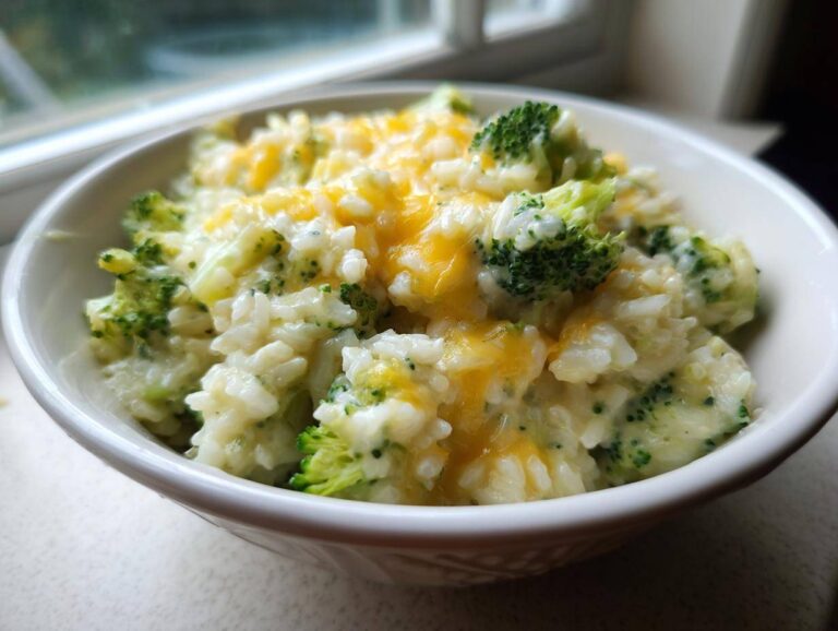 Close-up of a creamy bowl of broccoli rice topped with melted cheddar cheese.