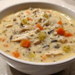 Close-up of a hearty bowl of creamy chicken wild rice soup with visible carrots and celery.