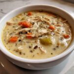 Close-up of a creamy chicken wild rice soup bowl with shredded chicken, carrots, and celery.