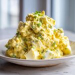 Close-up of a generous mound of creamy, yellow egg salad recipe garnished with fresh green chives.