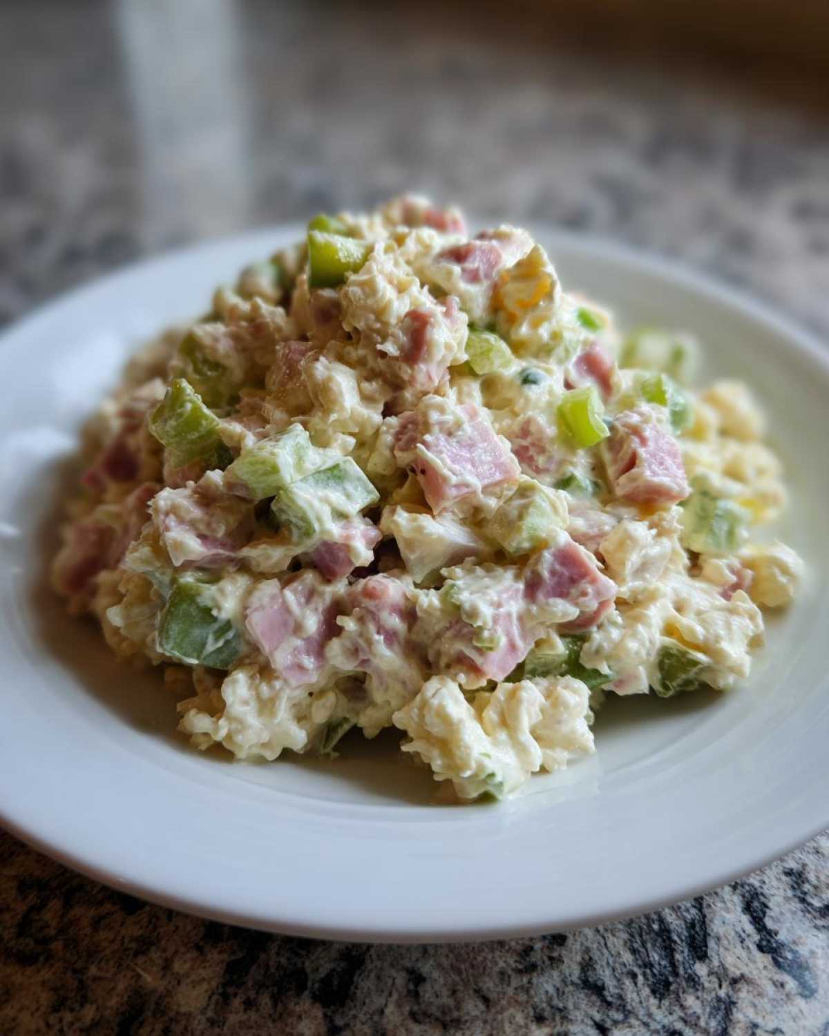 A scoop of creamy ham salad mixed with diced ham and green celery served on a white plate.