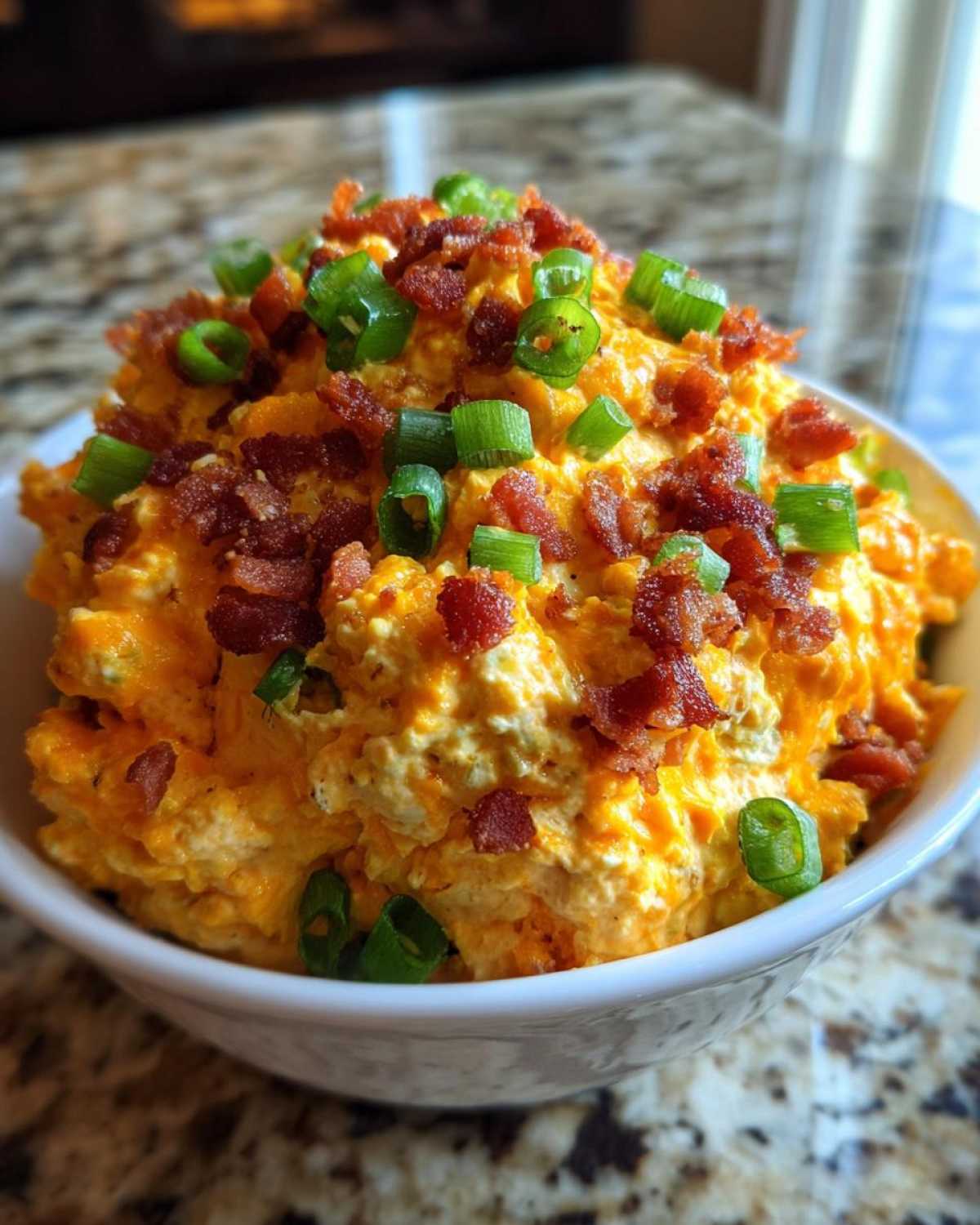 Close-up of creamy, orange million dollar dip topped generously with crispy bacon bits and fresh green onions.