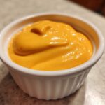 Close-up of thick, vibrant orange nacho cheese sauce served in a small white fluted ramekin.