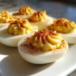 Close-up of creamy, piped deviled eggs sprinkled with paprika on a white plate.