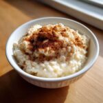 A close-up of creamy rice pudding topped generously with ground cinnamon in a white bowl.