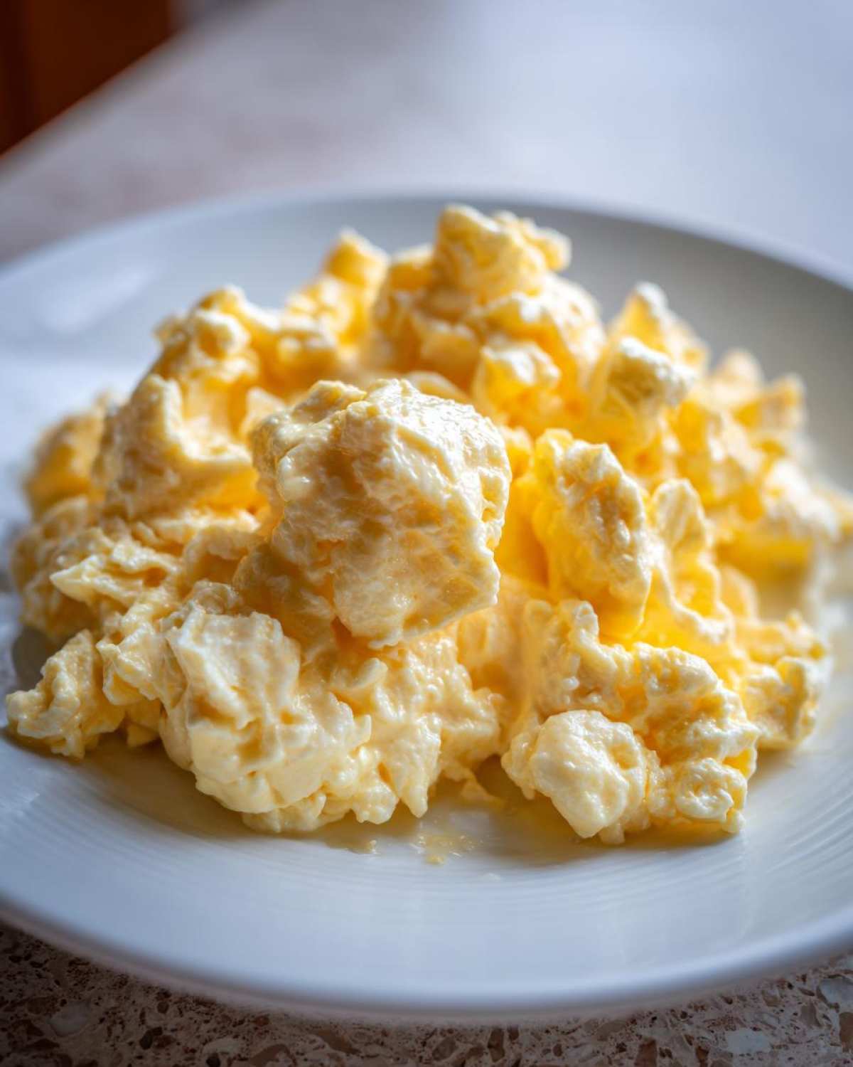 Close-up of perfectly cooked, creamy scrambled eggs piled high on a white plate.