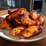 A pile of golden brown, crispy air fryer chicken wings stacked on a white plate.