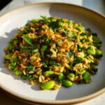 A close-up of a serving of crispy rice salad mixed with bright green edamame beans and fresh chopped mint and parsley.