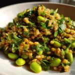 Close-up of a vibrant crispy rice salad mixed with bright green edamame beans and fresh parsley.
