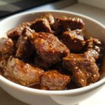 Close-up of tender, saucy crockpot steak cubes sprinkled with sesame seeds served in a white bowl.