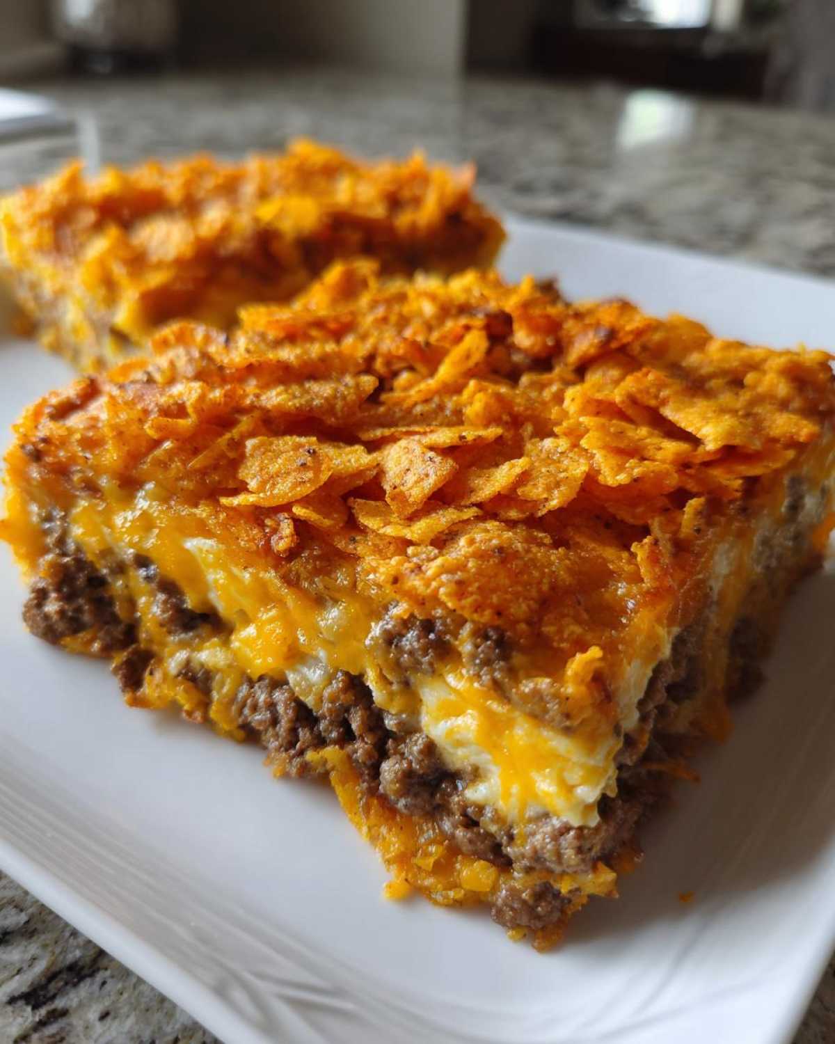 A close-up slice of Dorito Casserole showing layers of seasoned ground beef, cheese, and a crunchy Dorito topping.