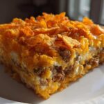 A square slice of rich Dorito Casserole featuring layers of ground meat, cheese, and a crunchy Dorito topping.