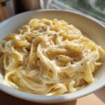 A close-up of fettuccine pasta coated in rich, creamy homemade alfredo sauce and topped with cracked black pepper.