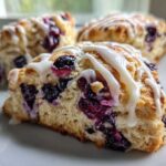 Close-up of a flaky blueberry scone drizzled with white vanilla glaze, showing juicy blueberries inside.