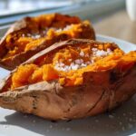 Two halves of a perfectly baked sweet potato with fluffy orange flesh topped with flaky sea salt.