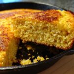 Close-up of a slice of golden buttermilk cornbread being lifted from a black cast iron skillet.