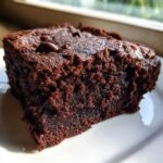 A close-up, rich, dark chocolate slice of fudgy sweet potato brownies sitting on a white plate.