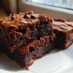 Close-up of fudgy sweet potato brownies stacked on a white plate, topped with melted chocolate chips.