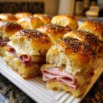 Close-up of freshly baked Ham and Cheese Sliders with melted cheese and poppy seed topping on a white platter.