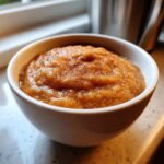 Close-up of a white bowl filled with thick, homemade applesauce topped with ground cinnamon.